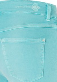Jean en denim bleu clair en gros plan montrant la poche arrière, la passants de ceinture et un petit logo cousu près de la taille.