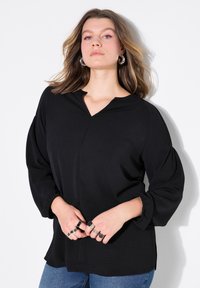 Maglietta nera a maniche lunghe con scollo a V, realizzata in tessuto testurizzato, con maniche a sbuffo e vestibilità rilassata, abbinata a jeans di denim blu.