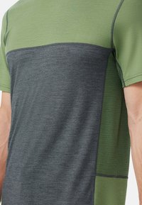 Kortärmad träningsskjorta med grön överdel, mörkgrå underdel, strukturerade meshsidopaneler och platta sömmar för komfort.