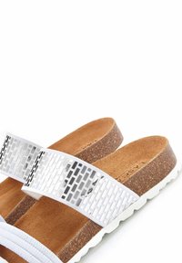 Witte verstelbare sandalen met een geweven zilveren band, kurken voetbed en witte zool. Textuur aan de oppervlakte met een gladde afwerking op de band.