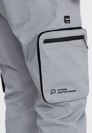 Pantaloni performanti grigi con tasca laterale con zip, hardware nero, texture sottile e dettaglio logo sulla coscia.