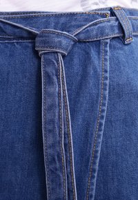 Džínové šortky s uzlovým páskem, v krásné středně modré barvě, viditelným prošíváním a hladkou texturou. Detailní pohled na pas.