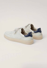 Zapatillas de cuero blancas con acentos en el talón de color azul marino, punta redonda, suela plana beige y detalles perforados en los laterales. Cierre con cordones.