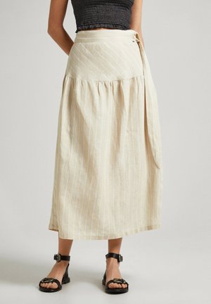 Jupe portefeuille beige à fines rayures verticales, portée avec des sandales noires et un top court noir, montrée de la moitié du torse jusqu'aux pieds.