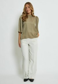 Light olive green blouse with short puff sleeves, featuring a round neckline. Paired with cream wide-leg trousers and black shoes.