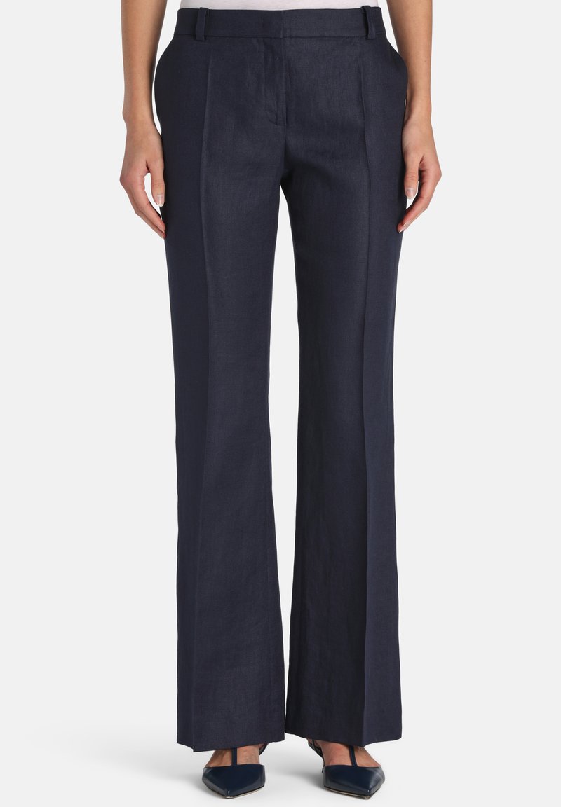 Pantalon large bleu marine avec plis à l'avant, poches latérales, passants pour ceinture, porté avec des talons noirs à bout pointu.