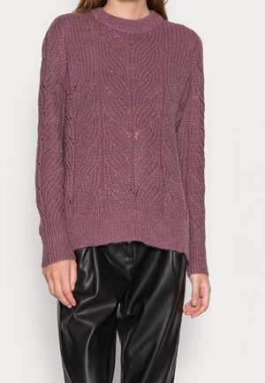 Knitted sweater in mauve with intricate cable patterns, ribbed neckline, and cuffs. Paired with loose-fitting black leather pants.