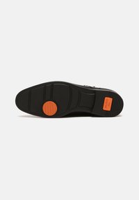 Suela de zapato de goma negra con patrones segmentados, superficie texturizada y un acento circular naranja cerca del centro etiquetado como "ALDO Flex."