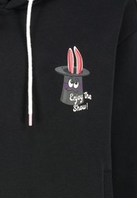 Zwarte hoodie met een cartoon-tovenaarshoed met konijnenoren, paarse band, grote ogen en de tekst "Geniet van de Show!" in het wit.