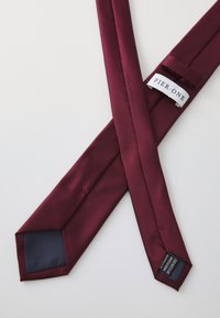 Cravate en soie bordeaux avec une texture lisse, extrémités pointues et une doublure intérieure bleu marine, comportant une étiquette blanche avec "PIER ONE."