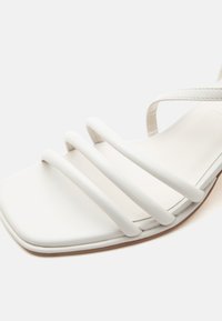 Λευκό σανδάλι με τρεις μαλακές λωρίδες πάνω από το πόδι και τετράγωνη μύτη σε επίπεδη σόλα.