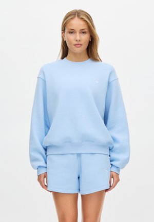 Niebieska bluza o luźnym kroju z prążkowanymi ściągaczami, zestawiona z dopasowanymi szortami. Bluza posiada dyskretne logo na piersi.