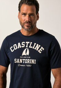 Námorní tričko s krátkým rukávem a kulatým výstřihem, s krémovým textem: "POBŘEŽÍ SANTORINI" a grafikou plachetnice. Vyrobeno z bavlny.