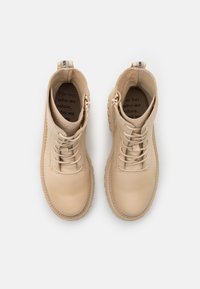 Beige lær ankle boots med snøredesign, rund tå og kraftig gummisåle. Innvendig har sålen trykt tekst.