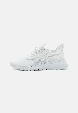 White athletic sneakers with a textured mesh upper, padded collar, and a thick, ribbed sole. Features tonal accents and lace-up closure.