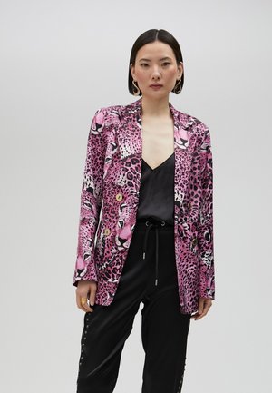 Ružové sako s leopardím vzorom, dlhými rukávmi, dvoma zlatými gombíkmi a hladkou látkou. Kombinované s čiernym topom a na mieru strihanými nohavicami.