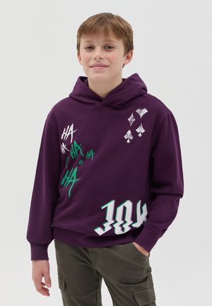 Sudadera morada hecha de una tela suave, con diseños gráficos en blanco y verde, que incluyen texto y patrones. El diseño incluye un bolsillo frontal.