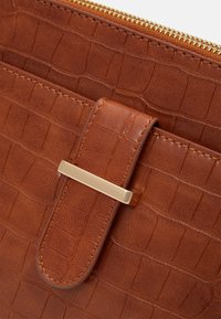 Brown leather bag featuring a crocodile texture, gold-toned hardware, and a secure flap closure with a metal accent. Zipper detail at the top.