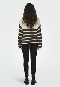 Maglione a righe in crema e marrone con maniche lunghe, texture a coste e vestibilità ampia, abbinato a jeans skinny neri e stivali.