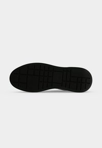 Semelle de chaussure noire avec un motif de bande de roulement en forme de grille, vue du dessous sur un fond clair uni.