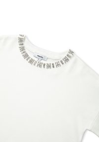 Sudadera blanca de manga corta con un escote redondo decorado con adornos metálicos. La etiqueta dice "IPEKYOL", tamaño 8. Textura suave.