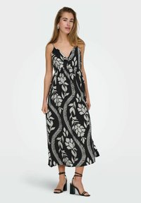 Zwarte maxi-jurk met een wit bladraster, verstelbare spaghettibandjes en een gathered taille. Gecombineerd met zwarte block-heeled sandalen.