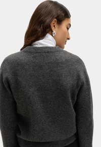 Gekürzter, dunkelgrauer Pullover mit weicher Textur und runder Ausschnitt, kombiniert mit einem weißen Rollkragenpullover darunter. Einfaches, minimalistisches Design.