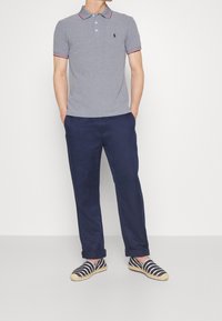 Grå polo shirt med röd och vit randig krage, marinblå byxor och randiga espadrillos. Avslappnad passform med en enkel logotypdetalj.