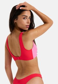 Color-blocked bikini set featuring a textured design with vibrant pink and red panels. The top has wide straps and a racerback style.