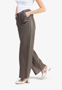 Pantalones de cuero sintético grises con un corte relajado, cinturilla elástica y bolsillos laterales, combinados con zapatos de tacón cuadrado en color crema.