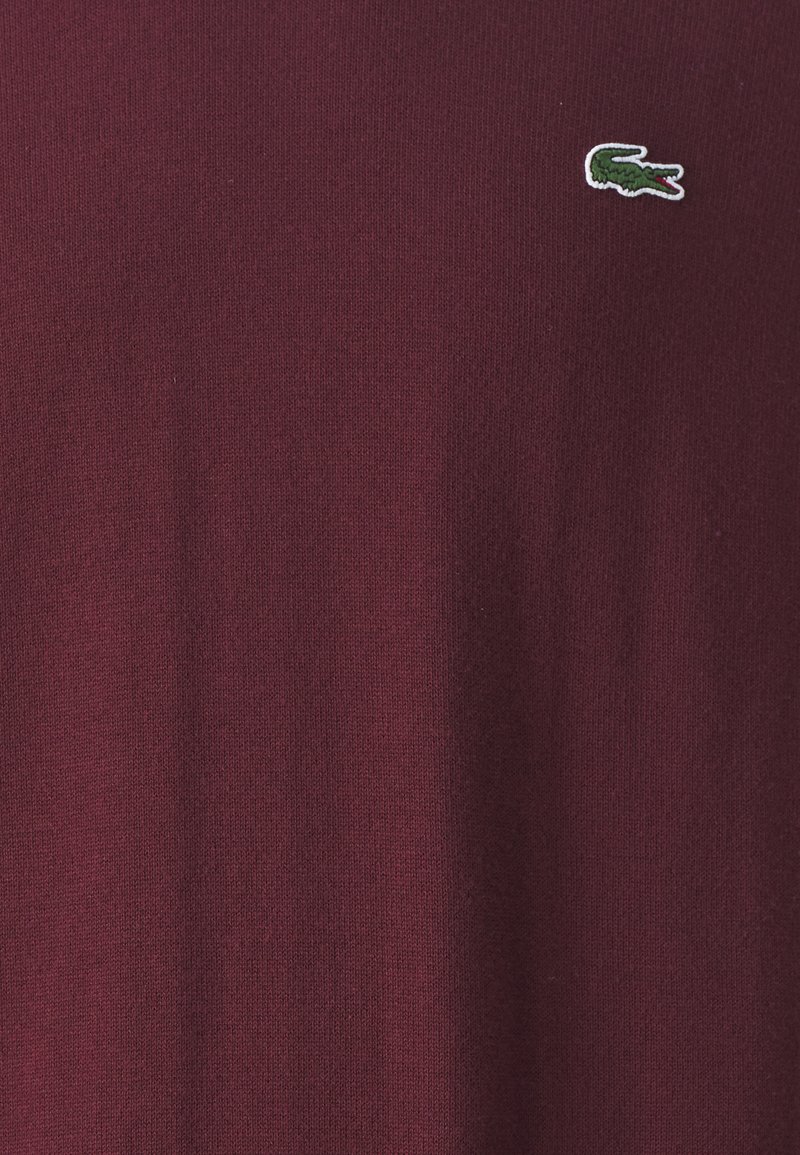Maglione a maglia bordeaux con un piccolo logo di coccodrillo ricamato in verde. Il tessuto ha una consistenza liscia e un classico collo a giro.