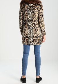 Kabát s leopardím vzorem a umělým kožíškem na límci, s dlouhým, rovný střihem. Kombinován s modrými džínami a černými teniskami.