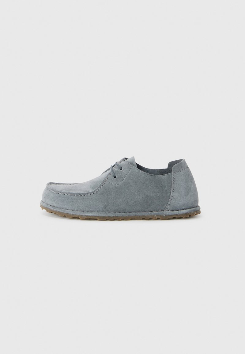 Gray suede shoes with a rounded toe, stitched detail, and a tan rubber sole. Laces and a low top design enhance accessibility.