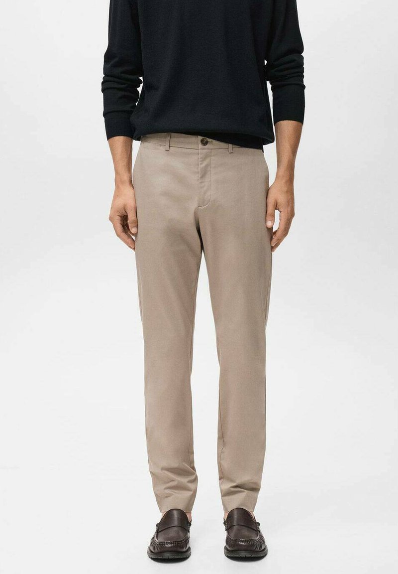 Beige Hosen mit geradem Bein, aus einem glatten Stoff gefertigt. Mit Knopfverschluss und seitlichen Taschen, getragen mit schwarzen Schuhen.