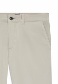 Beige Baumwollhose mit glatter Textur, ausgestattet mit einer Fronttasche und einem Knopfverschluss. Der Taillenbund hat ein kleines schwarzes Etikett.