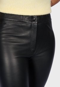 Zwarte leren broek met een gladde textuur, voorzien van een hoge tailleband, een ritssluiting aan de voorkant en een knoopsluiting.