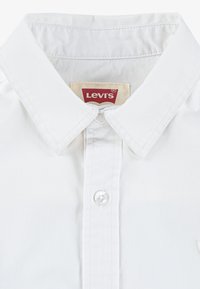 Camicia bianca Levi's con colletto classico, chiusura con bottoni trasparenti e etichetta con il marchio posizionata centralmente sul collo. Tessuto liscio e dettagli di cucitura.