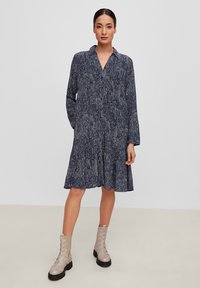 Abito navy con motivo floreale, maniche lunghe e colletto. L'orlo si allarga, abbinato a stivali alla caviglia grigi chiari. Tessuto morbido.