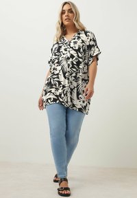 Svart och vit blommig skjorta med korta ärmar, lös passform och V-ringning som matchas med ljusblå skinny jeans och svarta sandaler.