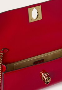 Bolso de mano de cuero rojo con un acabado brillante. Cuenta con un cierre dorado, detalle de cadena y un bolsillo interior con forro beige.