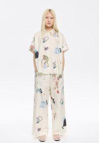 Completo a due pezzi composto da una camicia a maniche corte e pantaloni ampi. Tessuto di un leggero crema decorato con motivi e trame astratte colorate.