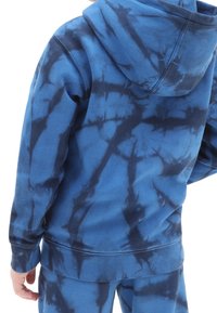 Sudadera azul con estampado tie-dye y patrones en azul oscuro, hecha de material suave. Presenta un bolsillo tipo canguro y una capucha con cordón.