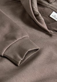 Brun hætte sweatshirt lavet af blødt bomuldsblanding. Har ribbede manchetter og en glat tekstur, med et mærke synligt indvendigt.