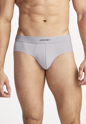 Männlicher Oberkörper und obere Beine, bekleidet mit hellgrauen Slip-Unterhosen mit "Jockey"-Logo am Bund, stehend mit entspannten Armen.