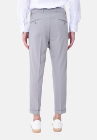 Pantaloni grigi su misura con una texture liscia, dotati di due tasche posteriori e risvolti. Abbinati a sneakers bianche.