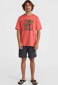 Camiseta de color coral con un estampado gráfico colorido, combinada con pantalones cortos de malla negros que presentan un logo. Los pantalones cortos tienen una cinturilla elástica.