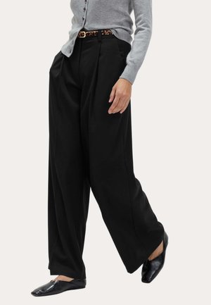 Pantaloni neri a gamba larga realizzati in tessuto morbido, caratterizzati da pieghe frontali e vita alta, abbinati a un cardigan lavorato a maglia grigio e scarpe basse nere.