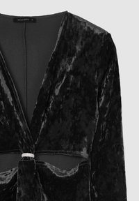 Schwarzes Samtkleid mit tiefem V-Ausschnitt und Wickeldesign, versehen mit einem dekorativen silbernen Ringakzent in der Taille und einer glatten Textur.