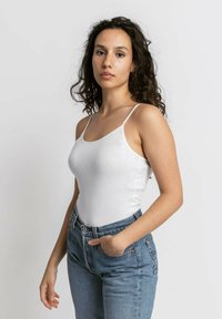 Witte katoenen tanktop met dunne bandjes, een aansluitend ontwerp, gecombineerd met hoge blauwe spijkerbroeken. Gladde textuur, minimalistische stijl.