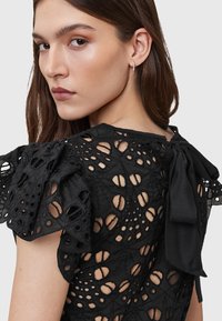 Black lace top featuring intricate cut-out patterns, puff sleeves, and a tied bow detail at the neck. Lightweight and textured fabric.
